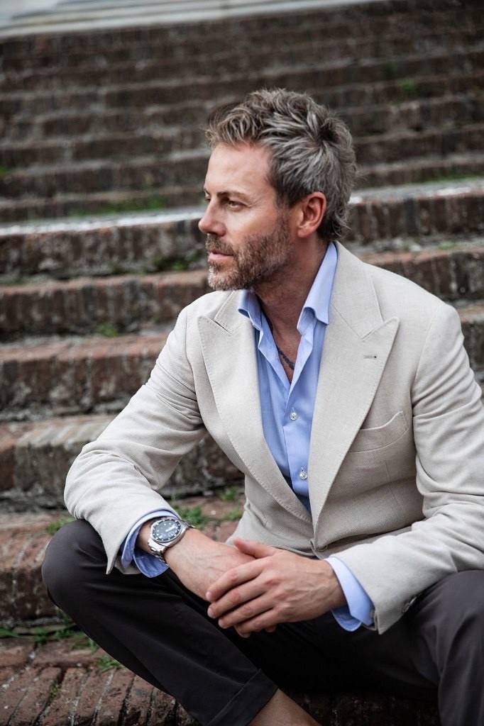 Gilberto Ramerini seated on stone steps, in a light blazer